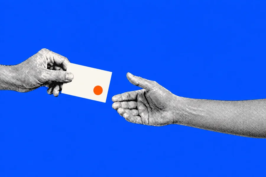 Een hand geeft een ivoren kaart met een oranje stip door aan een open hand op een kobaltblauwe achtergrond.